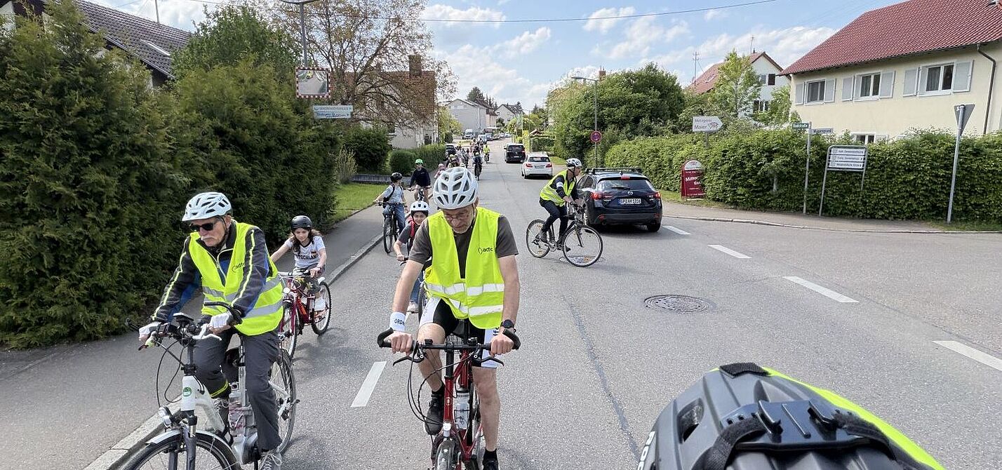 Fahrraddemo mit Kindern auf der Straße, vorneweg Ordner in gelben Westen, dahinter fahren Kinder