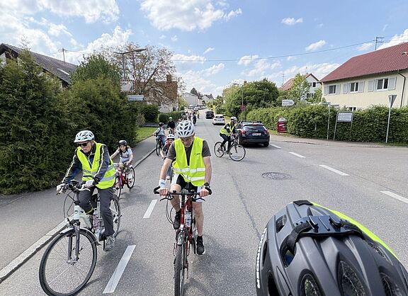 Fahrraddemo mit Kindern auf der Straße, vorneweg Ordner in gelben Westen, dahinter fahren Kinder